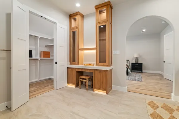 Built-in desk with lit glass cabinets, between a pantry and an arched doorway