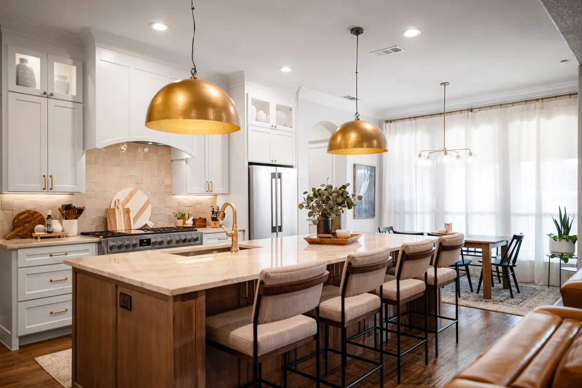 Remodeled kitchen with white cabinetry, wood island and brass pendants
