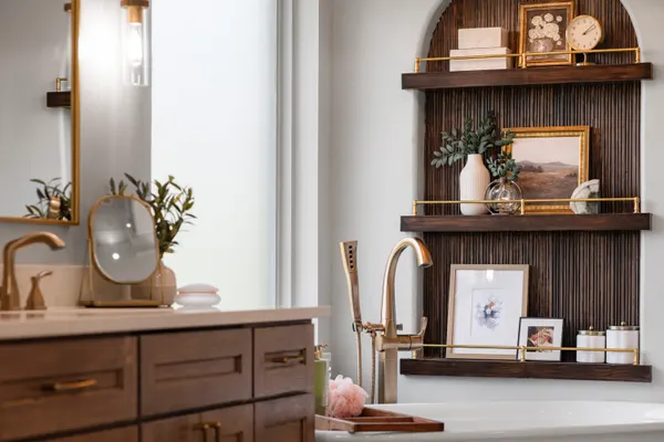 Arched niche of wood slats with brass rails, beside a brass tub filler