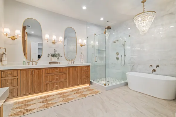 Primary bath with a wood vanity, twin oval mirrors, a freestanding tub and a glass shower