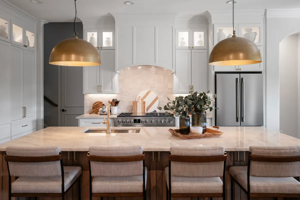 Knollwood kitchen island under brass dome pendants, with white cabinets to the ceiling beyond