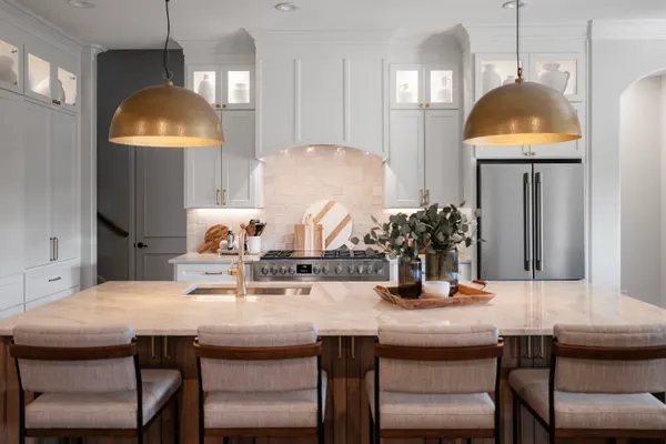 Kitchen island under brass dome pendants, with white cabinets to the ceiling beyond