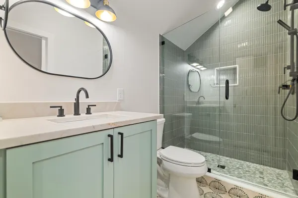 Bath with a sage green vanity and a green tile shower