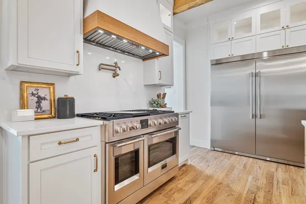 Professional-style range and pot filler under a wood-trimmed hood, beside a built-in refrigerator