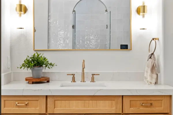 White oak vanity with brass fixtures and a brass framed mirror