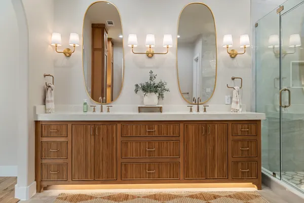 Primary vanity lit from below, with twin oval mirrors and brass sconces