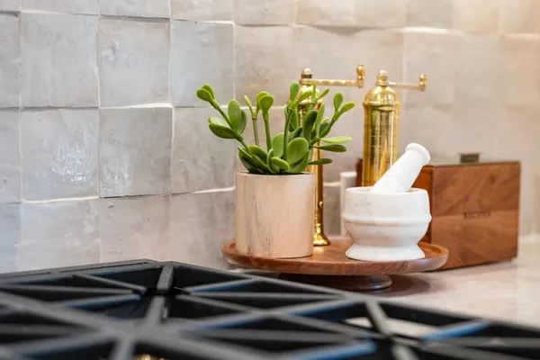 Brass pepper mill and a plant against the cream tile backsplash
