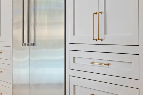 Built-in refrigerator beside white cabinets with brass pulls