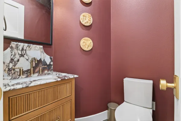 Powder room with burgundy walls, a fluted wood vanity, a veined stone backsplash and a brass faucet