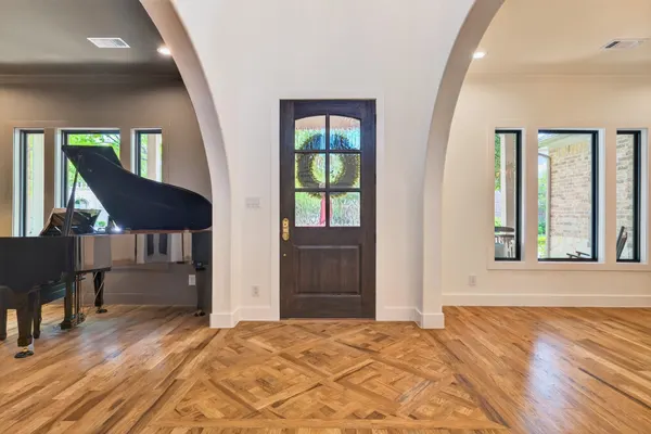 Entry under two arches, with a wood front door and a wood floor laid in a pattern