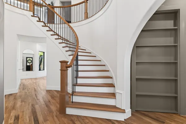 Curved stair with wood treads and black balusters, beside a gray bookcase set in an arched opening