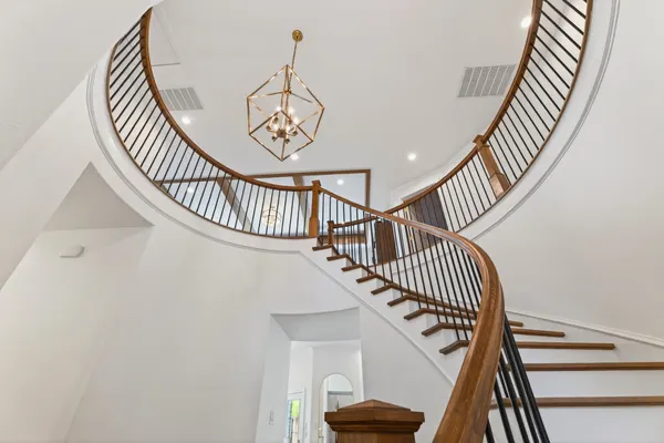 The curved stair and its wood handrail from below, under a gold lantern