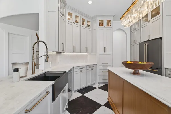 Black farmhouse sink and brass faucet beside the wood island, with lit glass-front cabinets above
