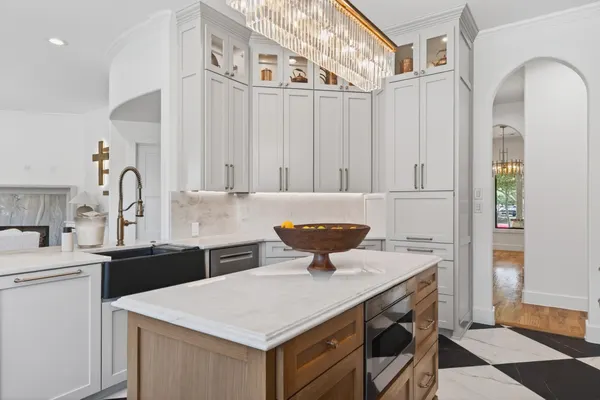 Kitchen island under a crystal chandelier, with white cabinets and an arched doorway beyond