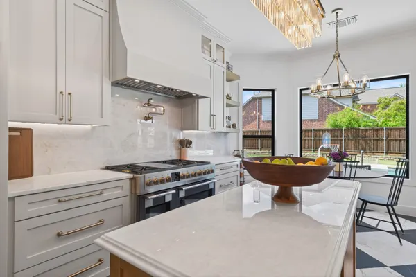 Professional-style range under a white range hood, with the breakfast table under a gold chandelier