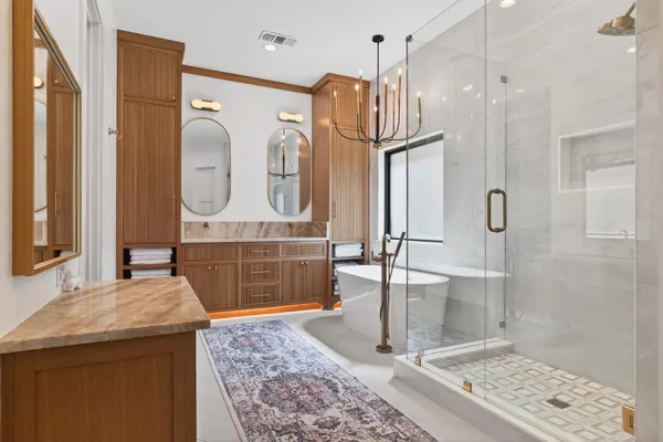 Primary bath with a wood vanity lit from below, a freestanding tub and a glass shower