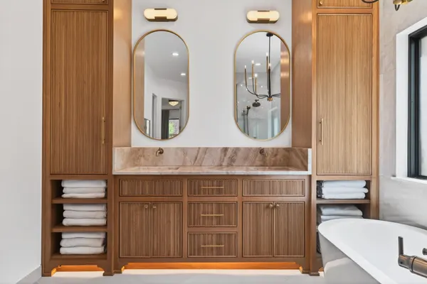 Wood double vanity with fluted doors, oval brass mirrors, a stone top and towel cubbies on each side
