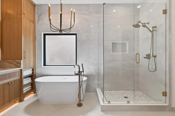 Freestanding tub under a black-framed window, beside a glass shower with brass fixtures