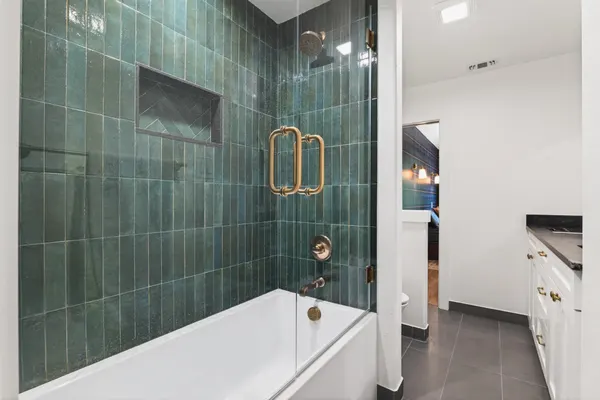 Tub and shower in deep green tile behind glass, with brass handles