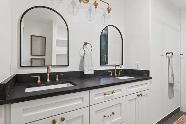 White double vanity with a black stone top, brass faucets and arched black mirrors