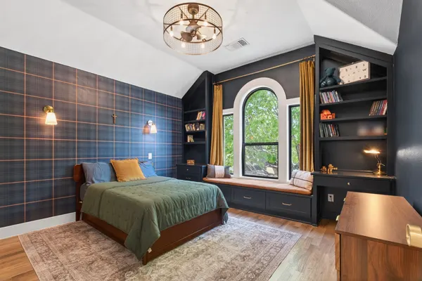 Bedroom with plaid wallpaper and dark built-in bookcases around an arched window with a window seat