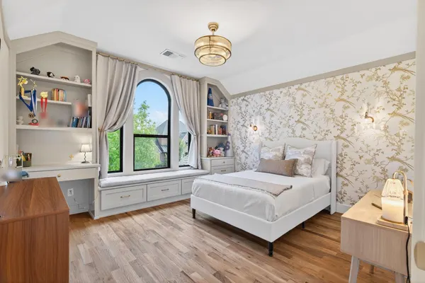 Bedroom with built-in shelves and a desk beside a window seat under an arched window