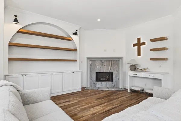Living room with a corner fireplace in a marble surround and floating wood shelves in an arched niche