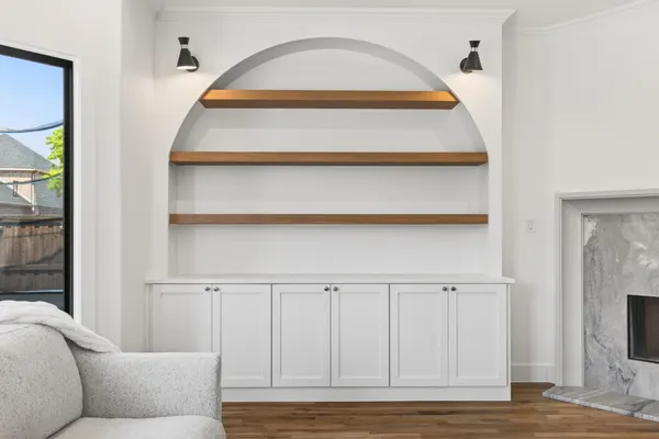 Arched niche with floating wood shelves over white cabinets, between black sconces