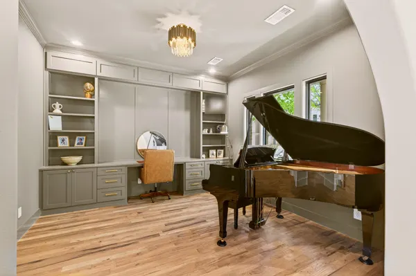 Study with built-in shelves and cabinets around a desk, beside a grand piano