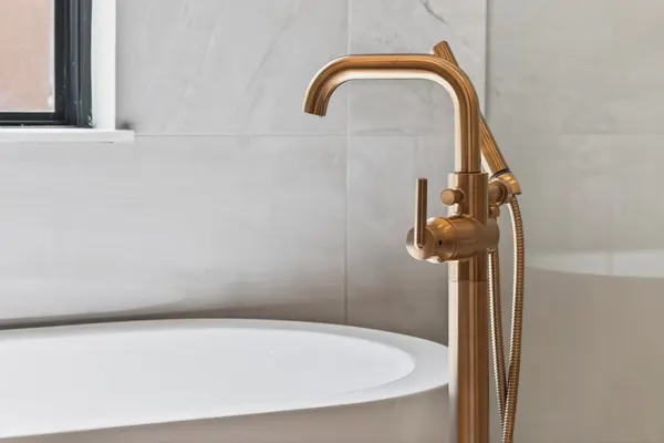 Brass floor-mounted tub filler beside the freestanding tub