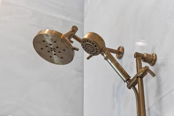 Brass rain showerhead and handheld shower on marble-look tile