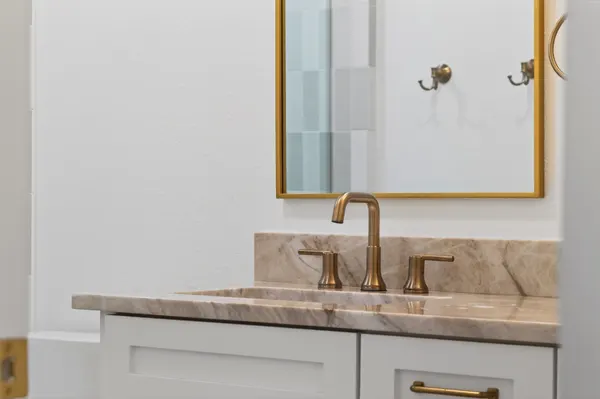 Brass faucet on a stone vanity top under a brass mirror