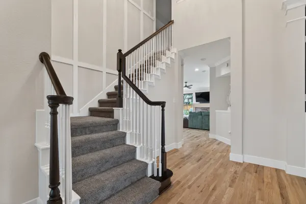 Carpeted stair with white balusters and a dark wood handrail, beside paneled walls