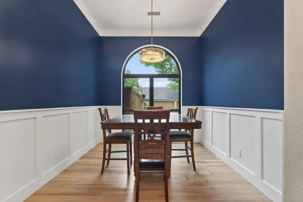 Dining room with navy walls over white wainscoting, an arched window and a chandelier