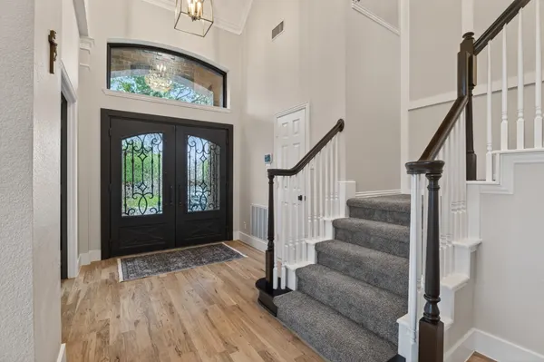 Entry with black iron double front doors under a transom window, beside the stair
