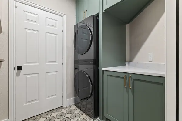 Laundry room with green cabinets, a stacked washer and dryer, and a patterned tile floor