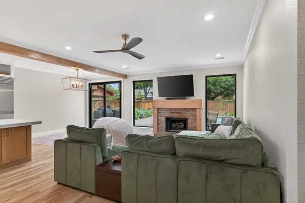 Living room open to the kitchen under a wood beam, with a brick fireplace