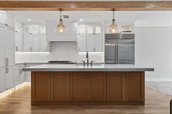 Wood island with a thick white countertop, under two glass pendants hung from a wood beam