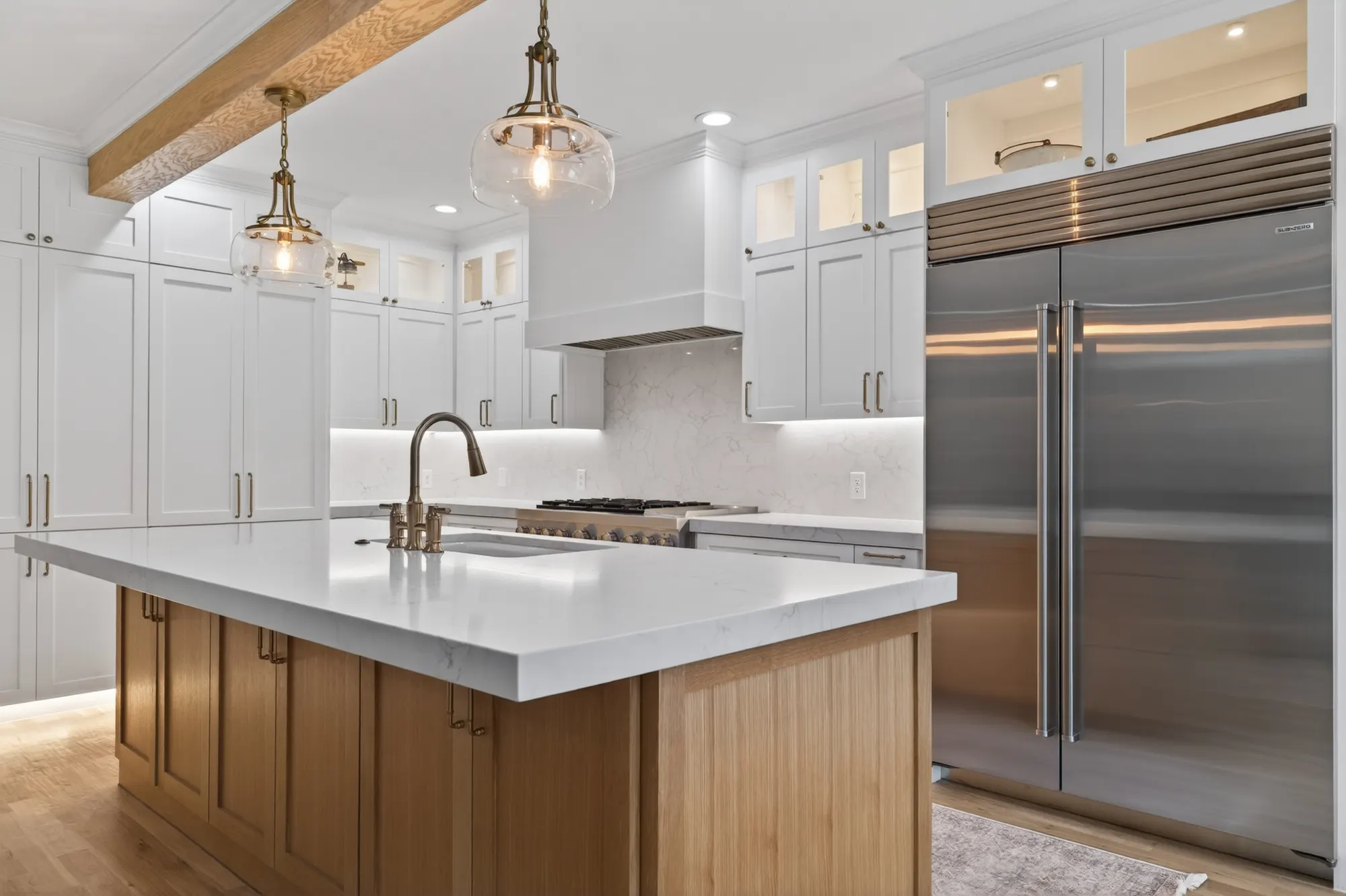 Kitchen with a wood island under glass pendants, white cabinets to the ceiling and a built-in stainless refrigerator
