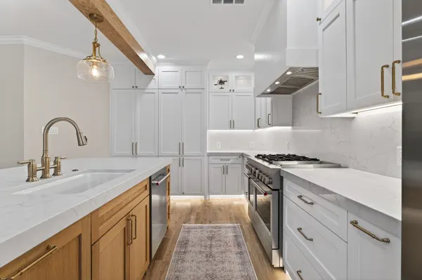 Island sink with a brass bridge faucet, facing the range wall, with lights under the cabinets