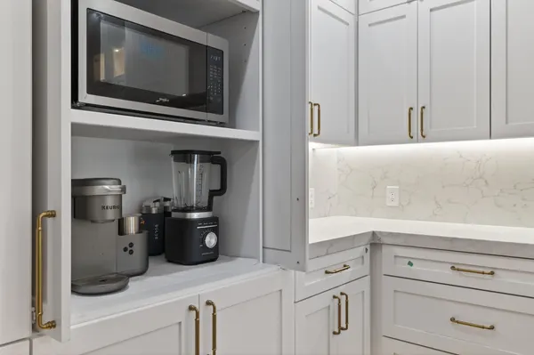 Tall cabinet holding the microwave and the coffee station, beside lit counters