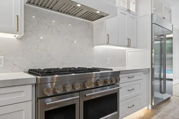 Professional-style range with double ovens under a white range hood, against a slab backsplash