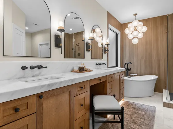Primary bath with a wood double vanity, arched black mirrors and a freestanding tub