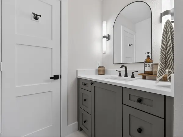 Bath with a gray vanity, a black faucet and an arched black mirror