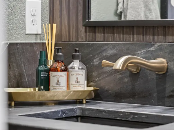 Brass wall-mount faucet over the dark stone counter and backsplash