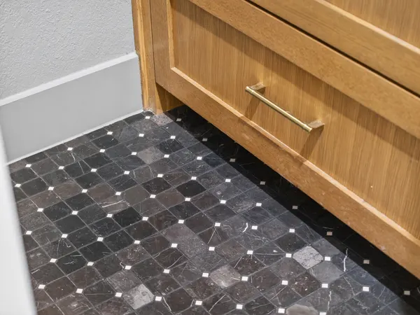 Dark mosaic tile floor under a wood vanity with a brass pull