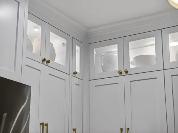 Glass-front upper cabinets, lit inside, over white cabinets with brass knobs