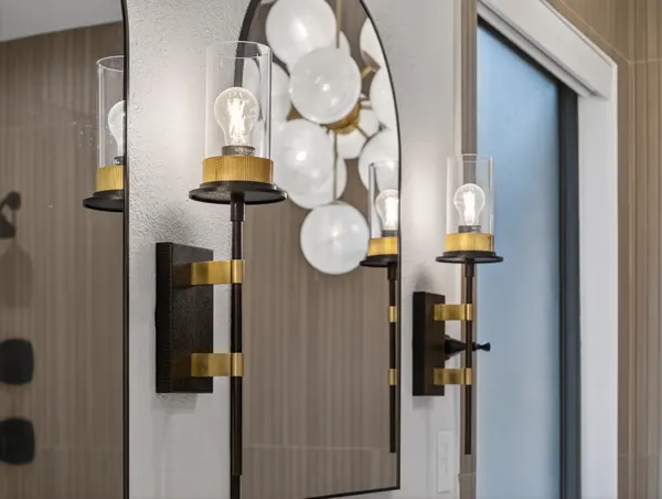 Black and brass sconce beside an arched mirror, with the globe chandelier behind