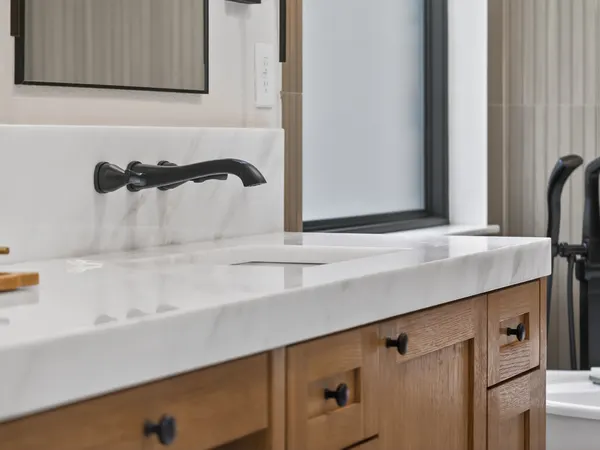 Matte black wall-mount faucet over a marble-look vanity top