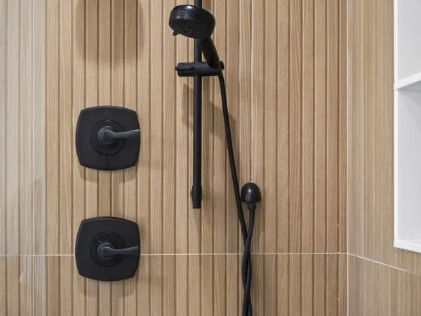 Matte black shower controls and a handheld shower on a slide bar, on fluted wood-look tile